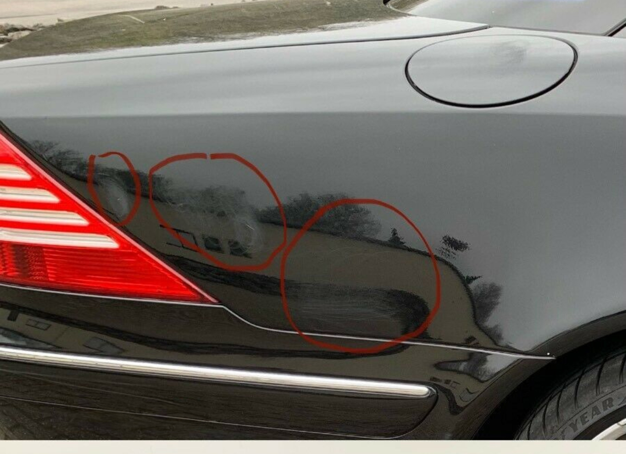 Verkratzter Lack am hinteren Kotflügel eines schwarzen Autos, mit sichtbaren Spuren und Beschädigungen im Lack.